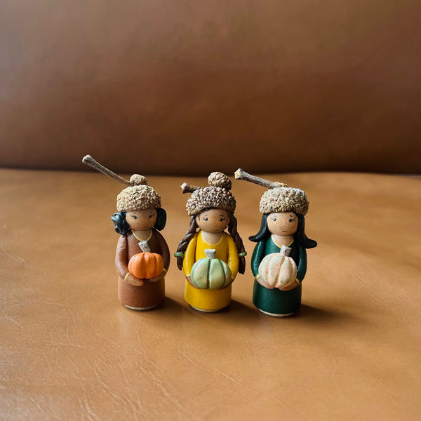 Three small figurines with autumn-themed accessories on a brown surface