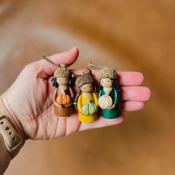 Three small figurines held in a hand against a brown background